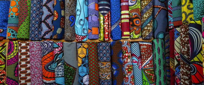 Rolls of colourful African wax-print fabric stacked on shelves.