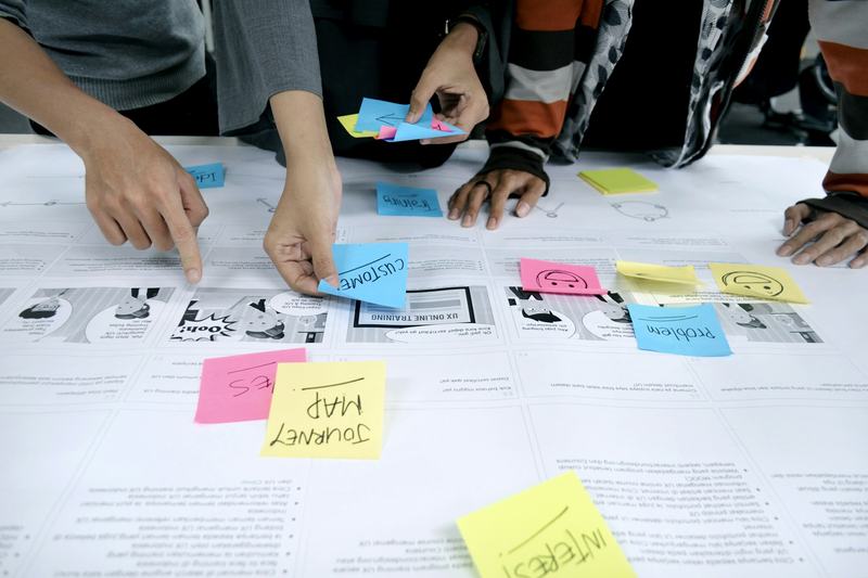 Several people’s hands arranging sticky notes on a table during a workshop.